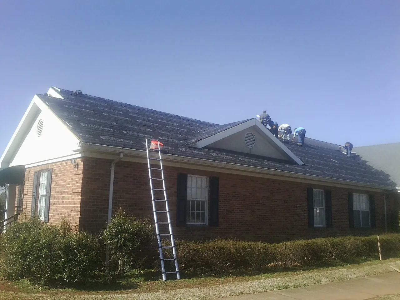 Crew tearing shingles off a brick ranch roof with a ladder set — Emergency Roof Repair work by our crew in Coal City