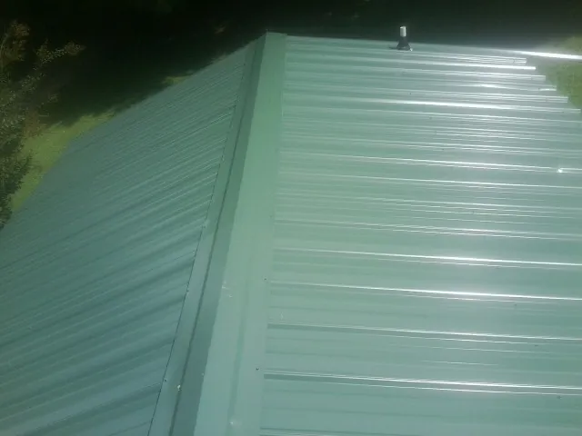 New green metal panels meeting at the ridge of a roof — Flat Roof Repair work by our crew in Coal City