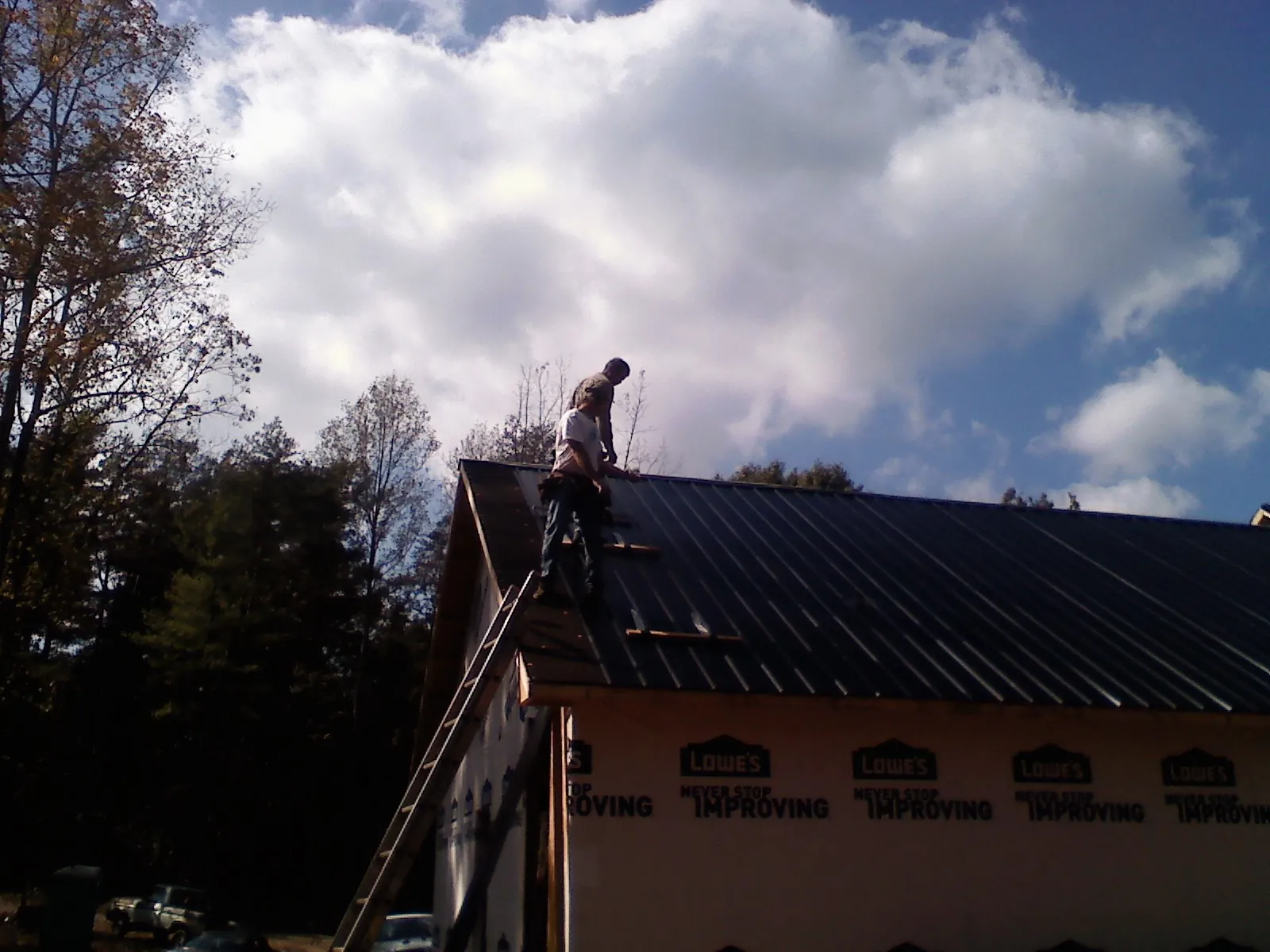 Roofer fastening dark metal panels high against a cloudy sky, from a Roof Inspection job in Coal City